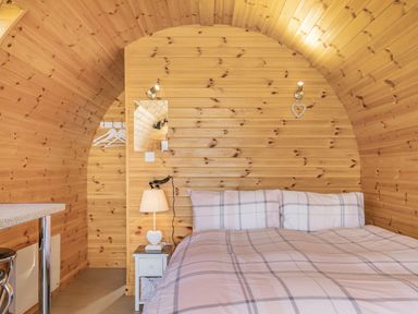 A bedroom with wooden walls a bed with checked bedding a bedside table with a lamp and hangers in Two Hoots Northop