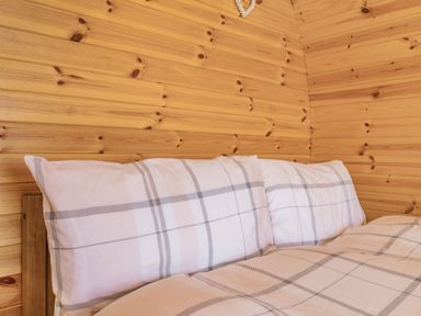 A bed with plaid pillows and a duvet in a wooden paneled room at Two Hoots in Northop
