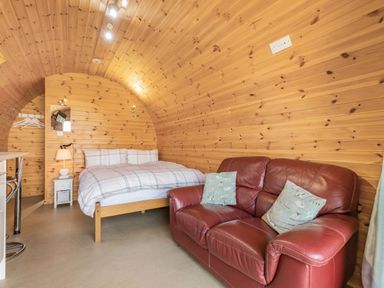 A bedroom with a bed and a red leather sofa in a wooden cabin at Two Hoots in Northop