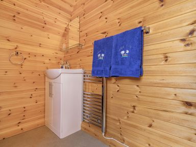 A bathroom with wooden walls a white sink cabinet a mirror a towel rail with blue towels at Two Hoots in Northop