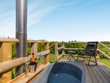 An outdoor deck with a hot tub a rocking chair a small table and a bottle of champagne with two glasses at Two Hoots in Northop