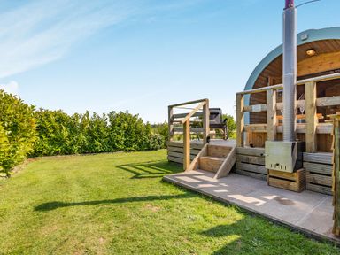 A wooden deck with steps and railing next to a curved wooden structure with a stove pipe in a garden at Two Hoots in Northop