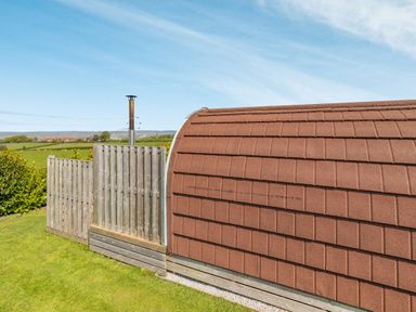 A curved brown roof structure with a wooden fence and outdoor countryside view at Two Hoots in Northop