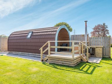 A small curved wooden cabin with a deck and fenced yard at Two Hoots in Northop