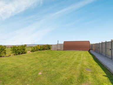 A fenced grassy backyard with a brown curved shed and a gravel path at Two Hoots in Northop