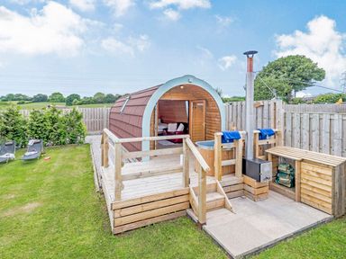 A wooden pod with a hot tub on a deck and lawn chairs on grass at Ewe Two in Oakenholt near Northop