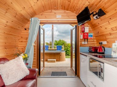 A wooden interior room with a red leather chair and kitchen appliances opening to an outdoor hot tub at Ewe Two in Oakenholt near Northop