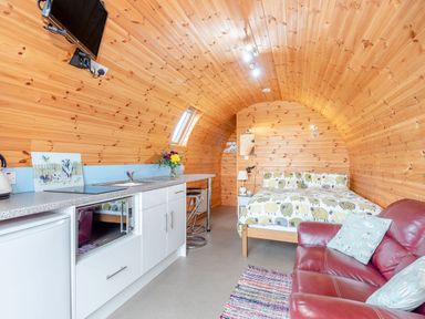 A wooden pod room with a kitchenette bed red sofa and a small rug at Ewe Two in Oakenholt near Northop