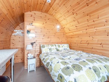 A wooden bedroom with a bed covered in sheep patterned bedding a nightstand with a lamp and a wall mirror at Ewe Two in Oakenholt near Northop