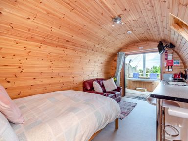 A wooden cabin interior with a bed a small red sofa a kitchen counter and a view of an outdoor hot tub at Ewe Two in Oakenholt near Northop