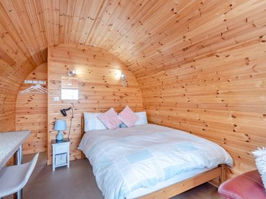 A bedroom with a bed, nightstand, mirror, and chair in a wooden cabin at Ewe Two in Oakenholt near Northop