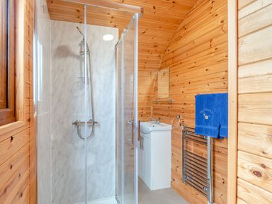 A bathroom with a shower cabin a sink with a mirror and a towel radiator with blue towels at Ewe Two in Oakenholt near Northop