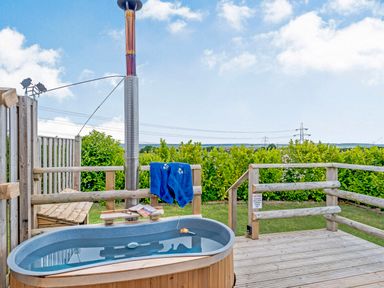 An outdoor wooden hot tub with blue towels hanging on a wooden railing and green bushes in the background at Ewe Two in Oakenholt near Northop