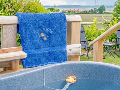 A blue towel on a wooden railing next to a hot tub with a floating thermometer in a garden at Ewe Two in Oakenholt near Northop