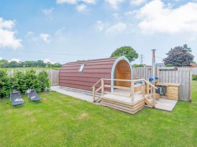 An outdoor area with a small wooden pod structure on a raised platform and two lounge chairs on grass at Ewe Two in Oakenholt near Northop