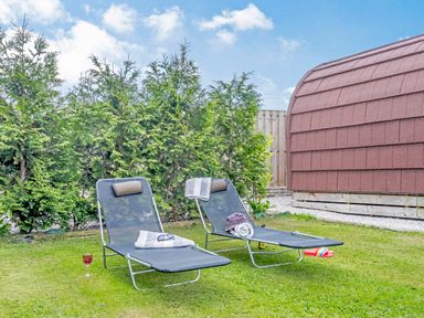 Two lounge chairs on a lawn with glasses and hats near a wooden shed with trees behind at Ewe Two in Oakenholt near Northop
