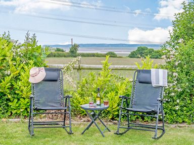 A garden with two black reclining chairs a small table with drinks and a bottle and a countryside view at Ewe Two in Oakenholt near Northop