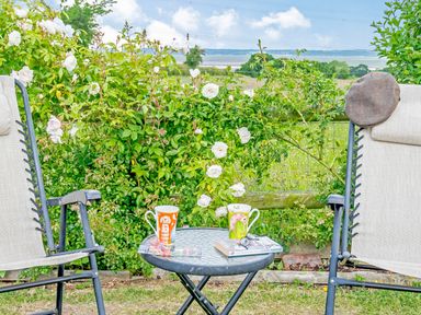 A garden seating area with two chairs and a round table with mugs and a book at Ewe Two in Oakenholt near Northop