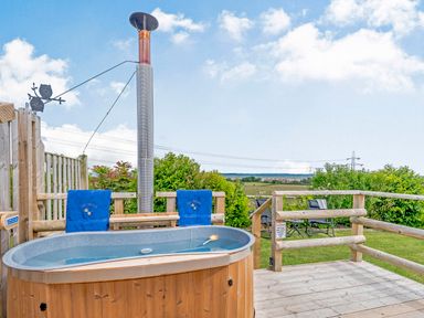 An outdoor wooden hot tub with blue towels on a deck overlooking fields at Ewe Two in Oakenholt near Northop