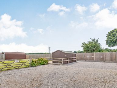 A gravel area with a wooden fence gate and two brown sheds near two trees at Ewe Two in Oakenholt near Northop