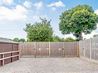 An outdoor gravel area enclosed by wooden fencing with trees beyond the fence at Ewe Two in Oakenholt near Northop