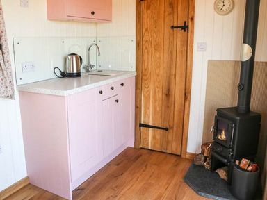 A kitchen area with a pink cabinet countertop kettle wooden door and wood-burning stove at Llety'r Bugail in Holyhead