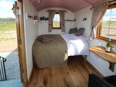A small bedroom with a double bed wood floors and a side table with wine and glasses at Llety'r Bugail in Holyhead