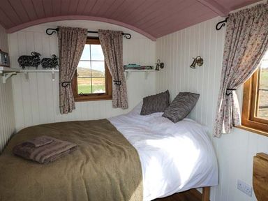 A bedroom with a double bed two windows with floral curtains and shelves with books and decorations at Llety'r Bugail in Holyhead