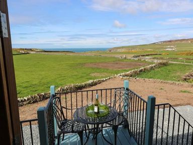 A balcony with a table and two chairs overlooking fields and distant sea at Llety'r Bugail in Holyhead
