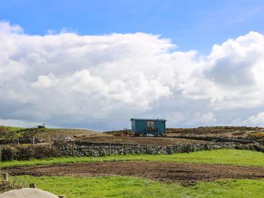 A small blue building on a grassy field with stone walls and a partly cloudy sky at Llety'r Bugail in Holyhead