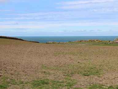A large plowed field with patches of grass and the sea in the background at Llety'r Bugail in Holyhead