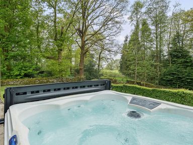 A hot tub with water in a garden area surrounded by trees and greenery at Elm - Woodland Cottages in Bowness-on-Windermere