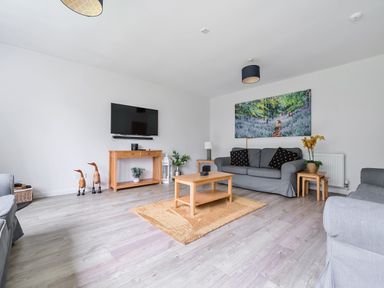 A living room with gray sofas wooden tables a wall-mounted TV and a painting at Elm - Woodland Cottages in Bowness-on-Windermere