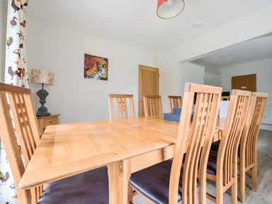 A dining room with a wooden table and chairs and a lamp on a side table at Elm - Woodland Cottages in Bowness-on-Windermere