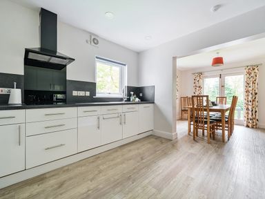 A kitchen with white cabinets and a dining area with wooden table and chairs at Elm - Woodland Cottages in Bowness-on-Windermere