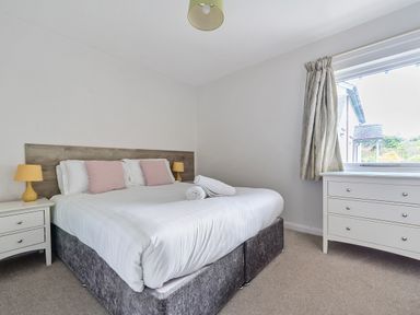 A bedroom with a double bed, two bedside tables with lamps, a dresser under a window and curtains at Elm - Woodland Cottages in Bowness-on-Windermere