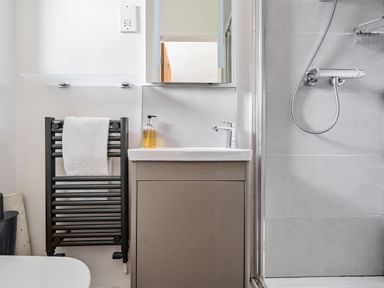 A bathroom with a small sink and cabinet a towel radiator with a white towel and a shower area Elm - Woodland Cottages Bowness-on-Windermere