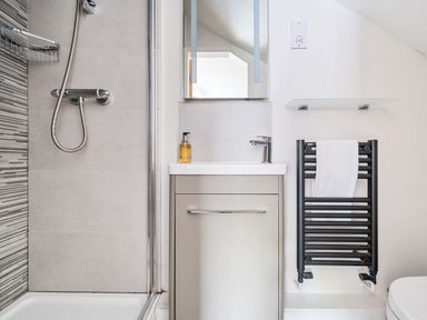 A bathroom with a shower area a sink with cabinet a mirror a towel rail with a white towel and a glass shelf at Elm - Woodland Cottages in Bowness-on-Windermere