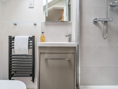 A bathroom sink with a cabinet and soap dispenser next to a towel rack and shower at Elm - Woodland Cottages in Bowness-on-Windermere