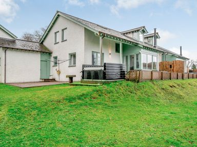 An exterior view of a white house with green trim a grassy lawn and a wooden fence at Cherry - Woodland Cottages in Bowness-in-Windermere