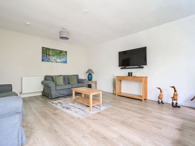 A living room with grey sofas a wooden coffee table a wall-mounted television and decorative wooden ducks at Cherry - Woodland Cottages in Bowness-in-Windermere
