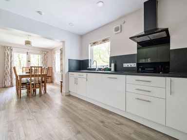 A kitchen with white cabinets a black countertop and a dining table with chairs at Cherry - Woodland Cottages in Bowness-in-Windermere