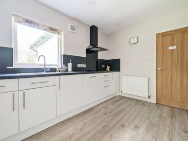 A kitchen with white cabinets black countertop a window above the sink and a wooden door at Cherry - Woodland Cottages in Bowness-in-Windermere