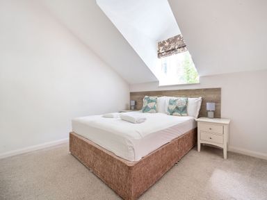 A bedroom with a bed with teal floral pillows bedside tables and a window at Cherry - Woodland Cottages in Bowness-in-Windermere