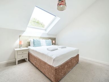 A bedroom with a bed under a skylight window and nightstands with lamps at Cherry - Woodland Cottages in Bowness-in-Windermere
