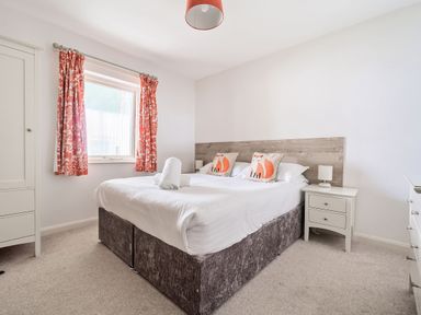 A bedroom with a double bed with white bedding fox pillows red patterned curtains and white furniture at Cherry - Woodland Cottages in Bowness-in-Windermere