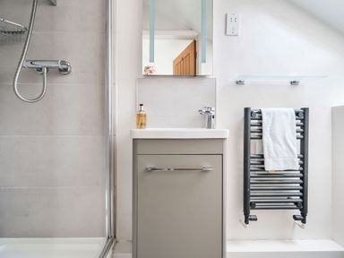 A bathroom with a shower, a sink with a cabinet, a mirror, a towel on a radiator at Cherry - Woodland Cottages in Bowness-in-Windermere