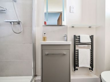 A bathroom with a shower area a sink with a cabinet a mirror and a heated towel rail with towels at Cherry - Woodland Cottages in Bowness-in-Windermere