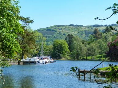 A lake with boats docked near trees and hills at Maple - Woodland Cottages in Bowness-on-Windermere