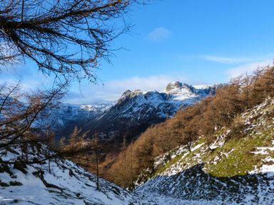 A mountain landscape with snow patches and leafless trees under a clear blue sky